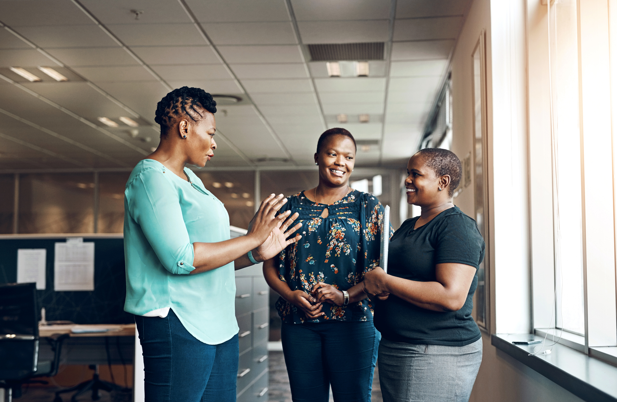 A group of three women are talking together in an office